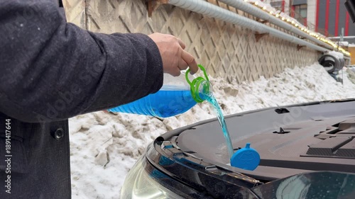 Male hands hold bottle of blue antifreeze, Pouring antifreeze liquid screen wash. man refills windshield wiper water on a car, Filling a windshield washer tank. Car repair, filling the washer fluid. 