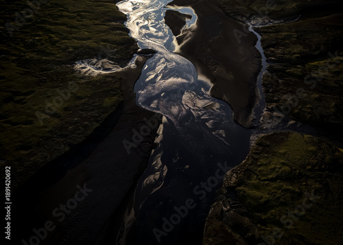 Aerial view of a dark river flowing through a rugged, moss-covered landscape, its silvery surface reflecting the sky above, Selfoss, Sveitarfelagid Arborg, Iceland.