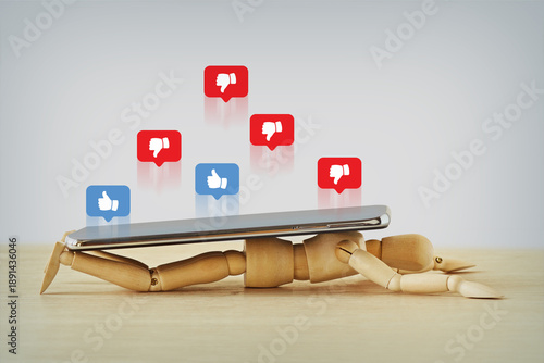 Wooden mannequin crushed under a smartphoe with like and dislike icons in speech bubbles - Concept of Social Media addiction and mental health