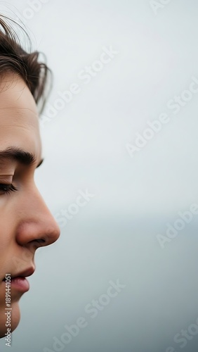 Young man with his hair in messy ponytail looks into the distance.