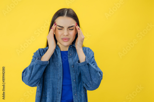 Young beautiful woman has headache, isolated on yellow background. Exhausted girl portrait