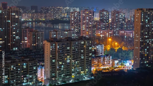 Xin Zhou, Wuhan, China city buildings glow with lights at night. Wuhan China cityscape at night showing illuminated apartment buildings and city lights