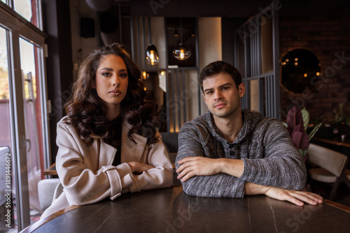 Unhappy young couple sitting in a café and looking at the camera
