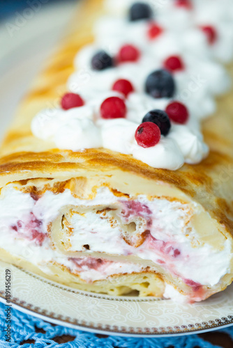 Homemade pancake roll called Finnish pancake with cream cheese and berry confit on table with blue lace tablecloth