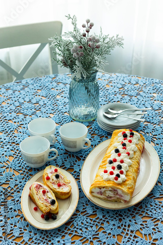 Homemade pancake roll called Finnish pancake with cream cheese and berry confit on table with blue lace tablecloth