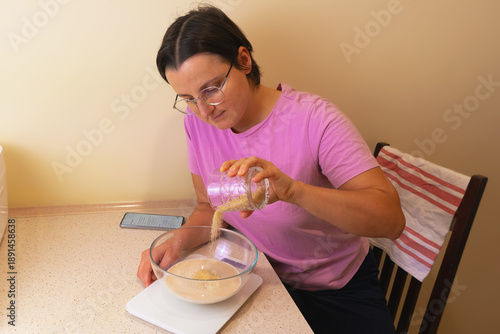 Female caucasian adult preparing dough in kitchen with phone recipe