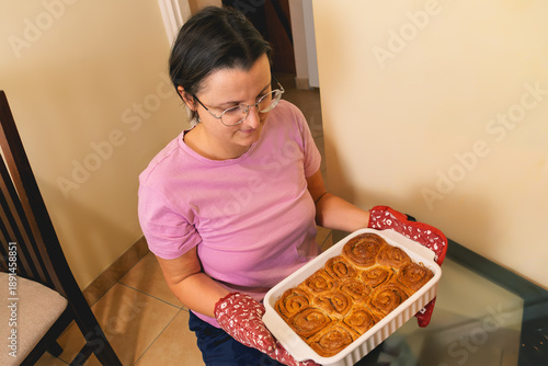 Caucasian female holding baked cinnamon rolls in kitchen setting