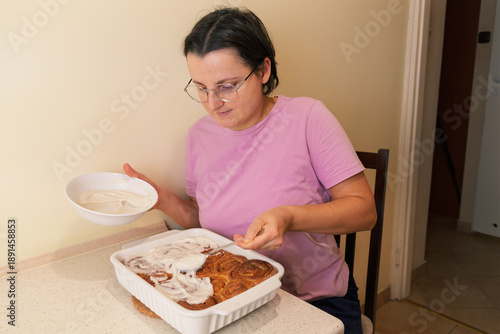 Caucasian female adult icing cinnamon rolls in kitchen