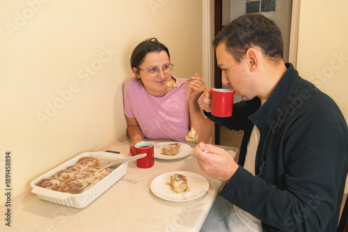 Caucasian adults enjoying cinnamon rolls and coffee in kitchen