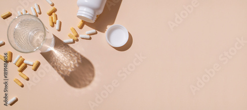 Photos Glass of water, white and beige vitamin capsules, supplements, or tablets on beige background, flat lay top view