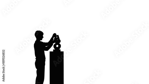 Silhouette of a person adjusting a sculpture in an art gallery.