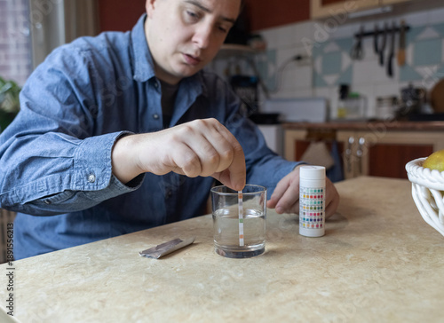 Wallpaper Mural A man in the kitchen tests tap water quality with a test strip. Home testing for drinking water safety, pH, chlorine, and chemical contaminants. Torontodigital.ca