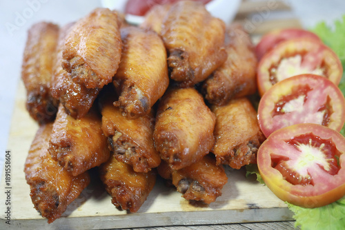Wallpaper Mural Crispy Chicken Wings Platter: A tempting close-up of golden-brown chicken wings on a wooden board. The dish is complemented by fresh tomato slices and fresh leaf. Torontodigital.ca