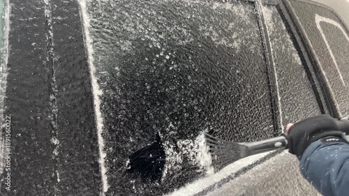 Person scraping thick ice and frost off car window with plastic ice scraper.  Winter routine, vehicle maintenance, safety, preparing for the commute.