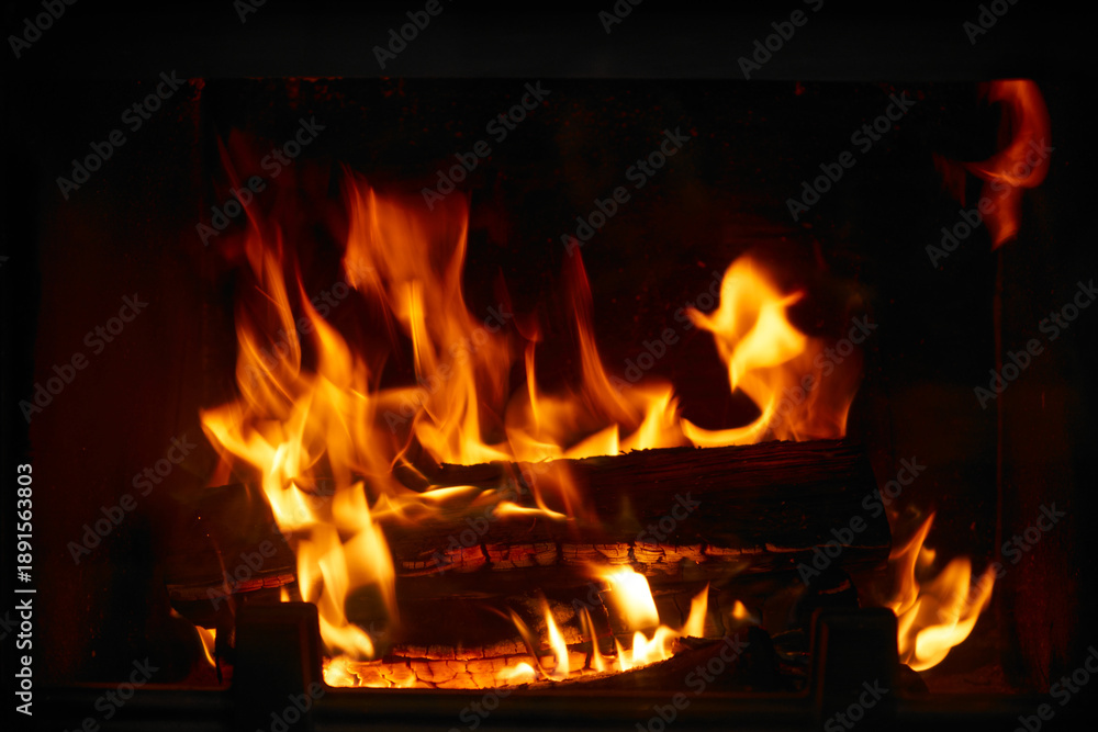 Obraz premium Fire burns in a fireplace during the evening, creating warmth and light in a cozy indoor space