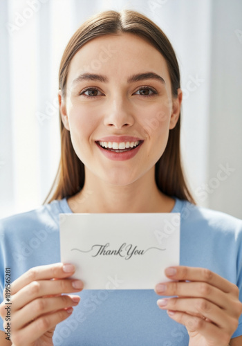 Smiling woman with long brown hair holds a thank you card in her hands, showcasing gratitude and warmth in a bright, inviting indoor setting with soft lighting