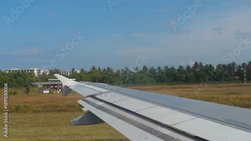 A view from an airplane window of the wing and the azure sea and tropical resort during taxiing to the runway.