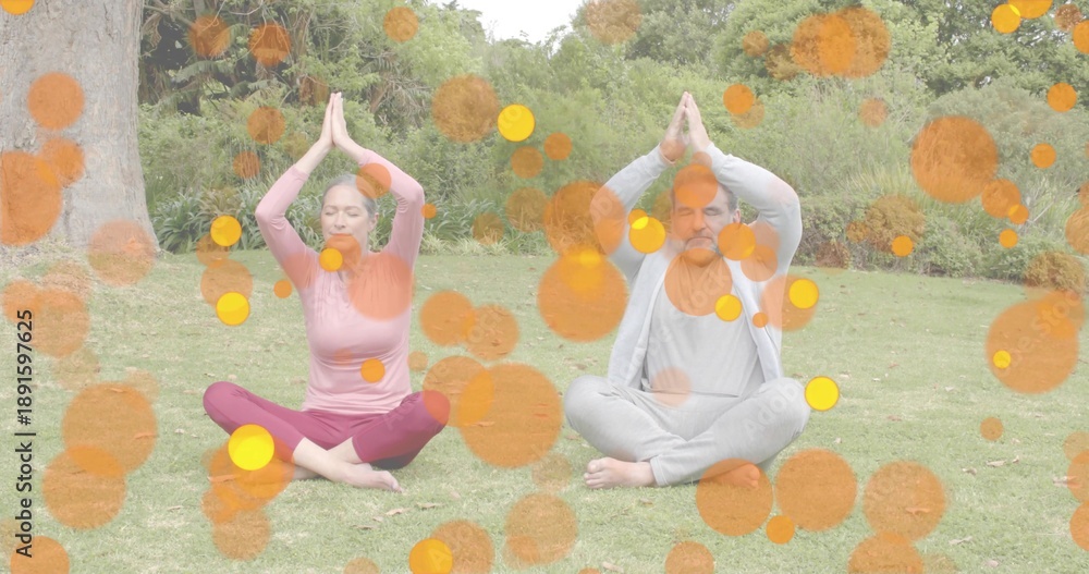 Fototapeta premium Meditating couple holding prayer pose on grass in park, wearing activewear with bokeh overlays