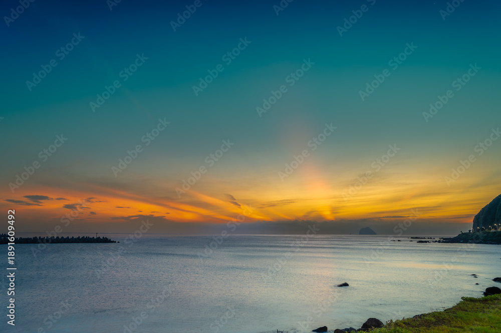 Obraz premium Witness the serene sunrise at Keelung Islet, Waishuangxi, Taiwan. Enjoy vibrant orange and blue skies with fast-moving clouds during a stunning summer morning.