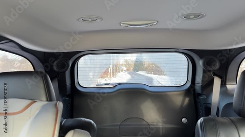 Interior View of Snowy Road Through Rear Car Window. Shot from inside back of moving vehicle looking out rear window at receding snowy road. Interior features black leather seats for cozy atmosphere.