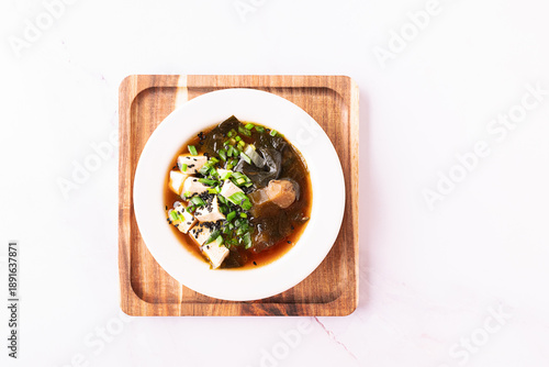 Fresh traditional miso soup with tofu, shiitake mushrooms, green onion, sea mustard and spices on white background with copy space for your design. Traditional Japanese cuisine. 