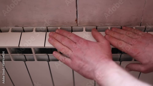 A man touches the cold radiators in his house. There is no heating in the apartment.