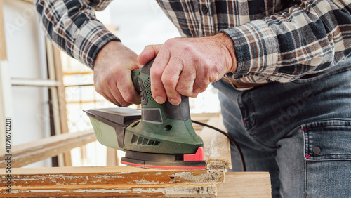 Craftsman. Adult carpenter using an electric sander to smooth an old wooden window. Construction industry, carpentry, housework do it yourself. Restoration.