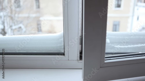 The window is opened for ventilation on a winter day. The window is covered with snow.