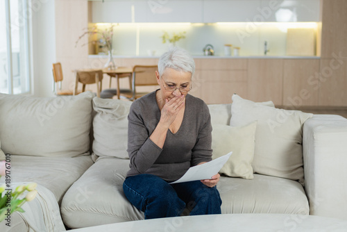 Sad tired ill sick lonely disappointed older senior woman reading bad news at home alone. Unhappy mature grandmother experiencing grief relative death. Stressed elder lady with paper document bill