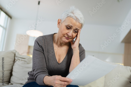 Sad tired ill sick lonely disappointed older senior woman reading bad news at home alone. Unhappy mature grandmother experiencing grief relative death. Stressed elder lady with paper document bill