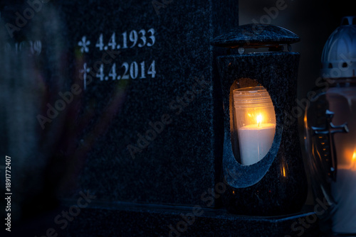 Lit burning candle at night on black stone monument with date birth and death in cemetery. Memory of the deceased. Expression of love