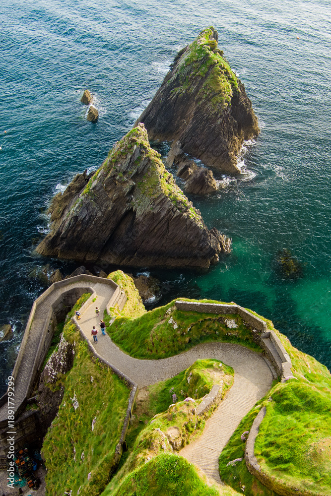 Fototapeta premium Dunquin or Dun Chaoin pier, Ireland's Sheep Highway. Aerial view of narrow pathway winding down to the pier, ocean coastline, cliffs. Popular location on Slea Head Drive and Wild Atlantic Way.