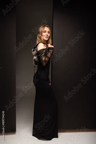 A girl in a black dress stands sideways and holds a bra in her hand.