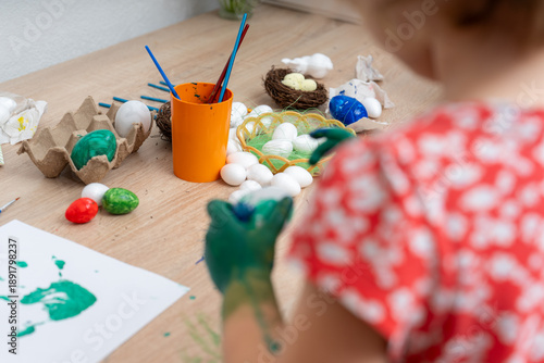 Obraz na płótnie Child paints colorful eggs at a small table while preparing for a holiday celebr