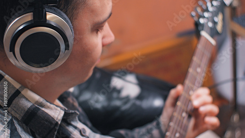 Φωτογραφία Side profile of a focused young man wearing headphones playing an electric guitar
