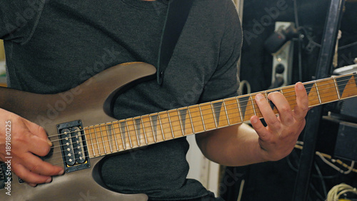 Close-up on a guitarist's hands playing a riff on a modern electric guitar. The shot captures the intense focus of a musician during practice or recording. Muted colors and studio setting