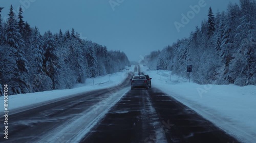 Car is driving on a frozen road in ice. Driver drives a car on a snowy highway in winter. Polar night in Arctic pine forest. Cold weather. Blizzard in winter journey, outdoor. Snowstorm in road trip.