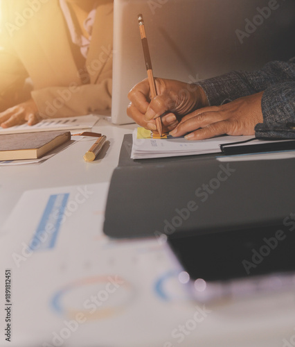 business documents on office table with tablet, smart phone and laptop and two colleagues discussing data