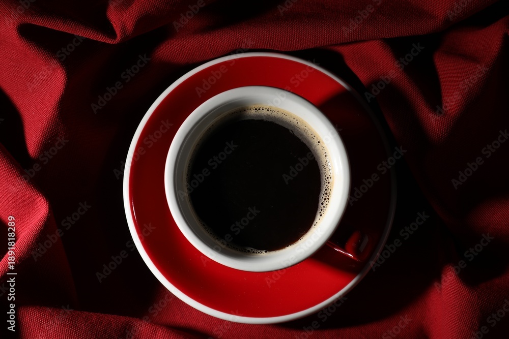 Naklejka premium Cup of aromatic coffee on red fabric, top view