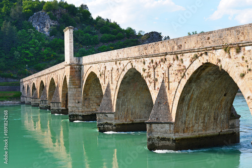 Scenic view of the historic Mehmed Pasha Sokolovic Bridge in Visegrad, Bosnia and Herzegovina, spanning the Drina River with natural mountain surroundings.