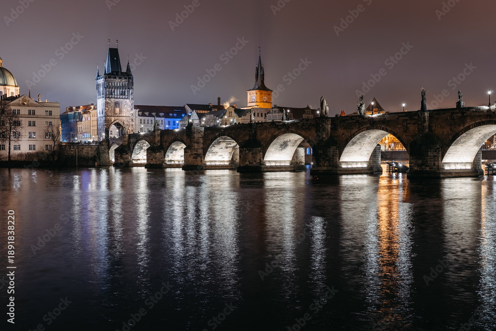 Obraz premium Charles Bridge at Night in Winter Viewed from Lesser Town Riverbank. Vltava River, tourists walking