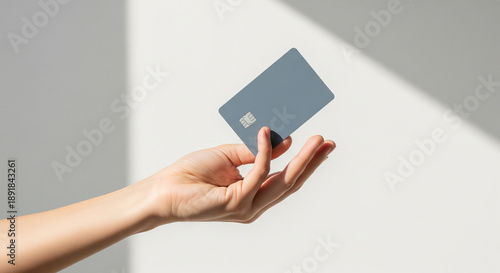 Minimalist Presentation of Blue-Gray Credit Card with Chip Held by Hand Against Soft Shadow Background Representing Modern Finance and Identity Verification