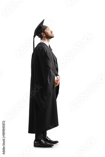 Full length shot of a man in a black graduation gown and cap looking up