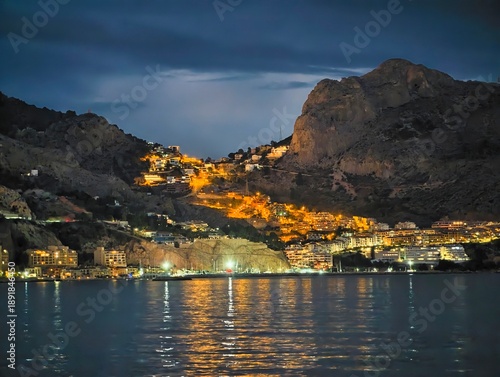 Village lights reflecting on water, Cozy hillside settlement shining across peaceful water surface at night