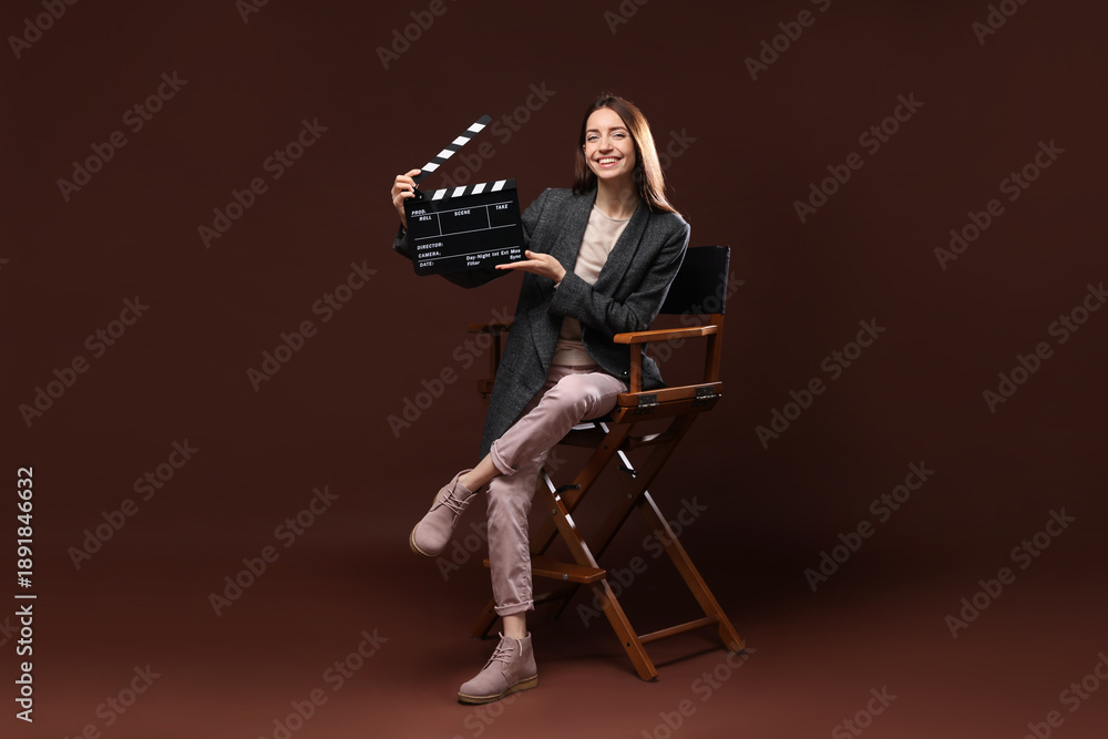 Fototapeta premium Professional film director with clapperboard on chair against brown background