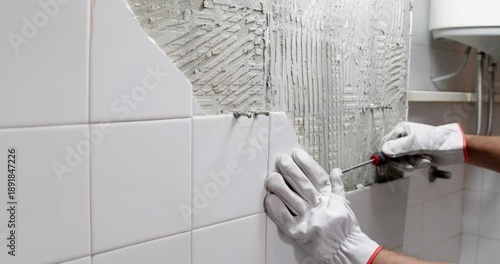 Construction worker demolishing and removing ceramic tiles in bathroom wearing protective gloves, close up