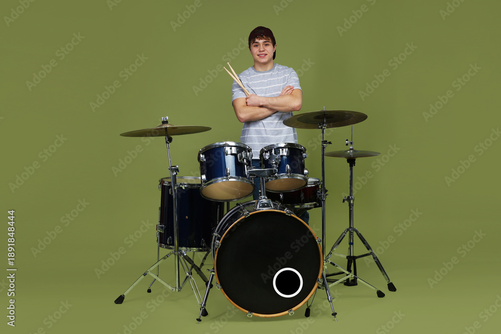 Fototapeta premium Smiling teenage boy in baseball cap with drumsticks and drum kit on green background