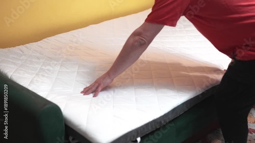 Man setting up a folding mattress  topper for sofa.  White quilted mattress for comfort sleeping on a couch.