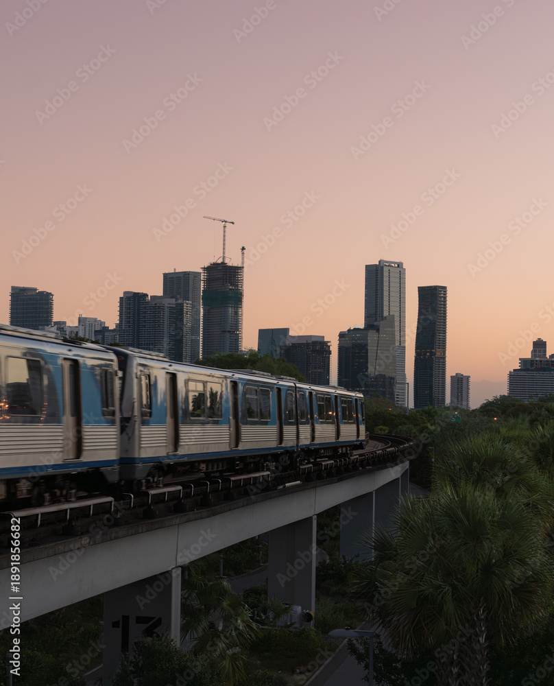 Obraz premium Urban metro train crossing elevated track with modern city skyline at sunset