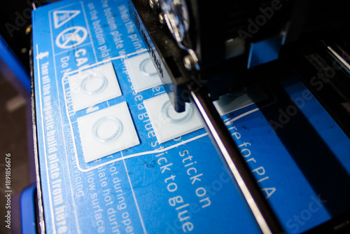 3D Printer Nozzle Printing Small Parts On Blue Adhesive Build Plate